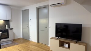 A modern kitchen with a built-in oven and a coffee maker, a flat-screen TV on a wooden stand, and a sliding door closet.