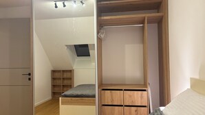 A bedroom with a wooden wardrobe, a bed, a desk, and a skylight.