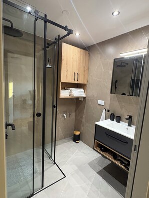 Een moderne badkamer met een douchecabine van glas, een houten wastafelmeubel en een spiegel boven de wastafel.