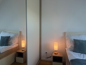 Een kamer met spiegels en twee bedden, elk met een nachtkastje en een lamp.
