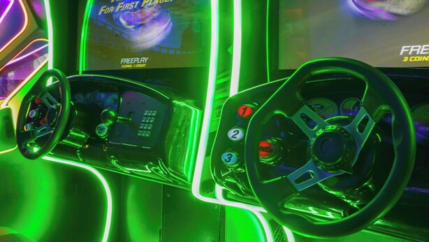 A gaming arcade with neon lights and racing game controls. - House of Wonder ✨ Theatre • Theme Rooms • Arcade • Pool • Minutes to Disney (Kissimmee)