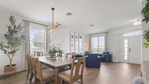 A spacious dining area with a wooden table and chairs, a chandelier, and a large window with curtains. - House of Wonder ✨ Theatre • Theme Rooms • Arcade • Pool • Minutes to Disney (Kissimmee)