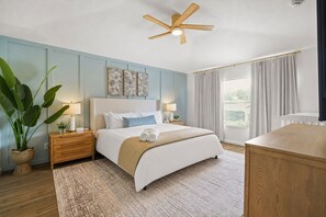 Ein Schlafzimmer mit Bett, Nachttische, Fenster mit Vorhängen und einer Zimmerpflanze.