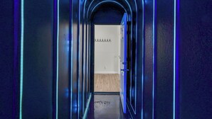 A narrow hallway with blue neon lighting, leading to a room with a wooden floor and a white door. - House of Wonder ✨ Theatre • Theme Rooms • Arcade • Pool • Minutes to Disney (Kissimmee)