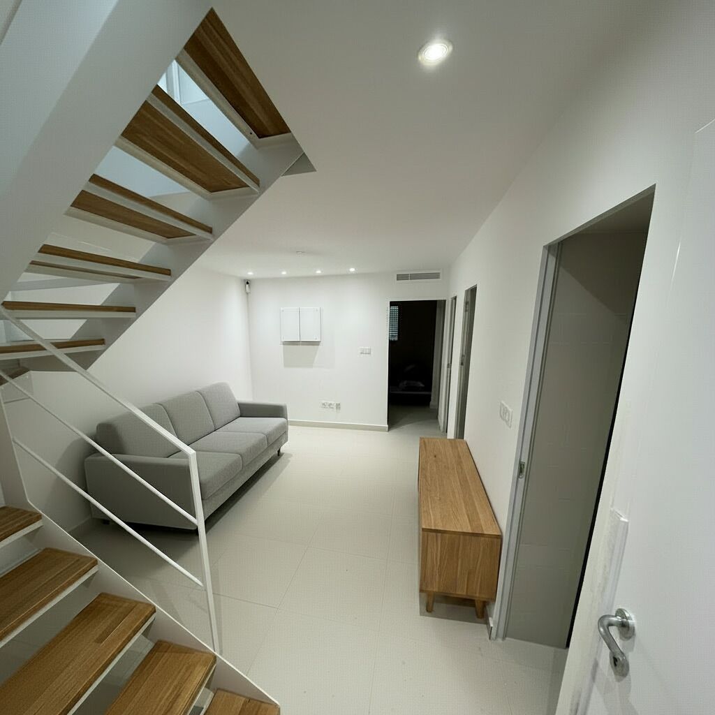 A modern interior with a staircase, a grey sofa, a wooden bench, and a door.