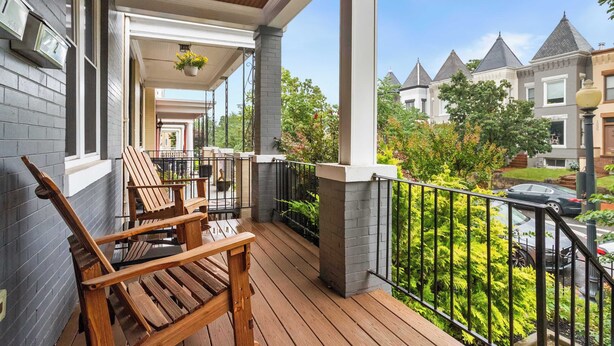 Eine Holzterrasse mit Adirondack-Stühlen, einer Veranda und Blick auf benachbarte Häuser.
