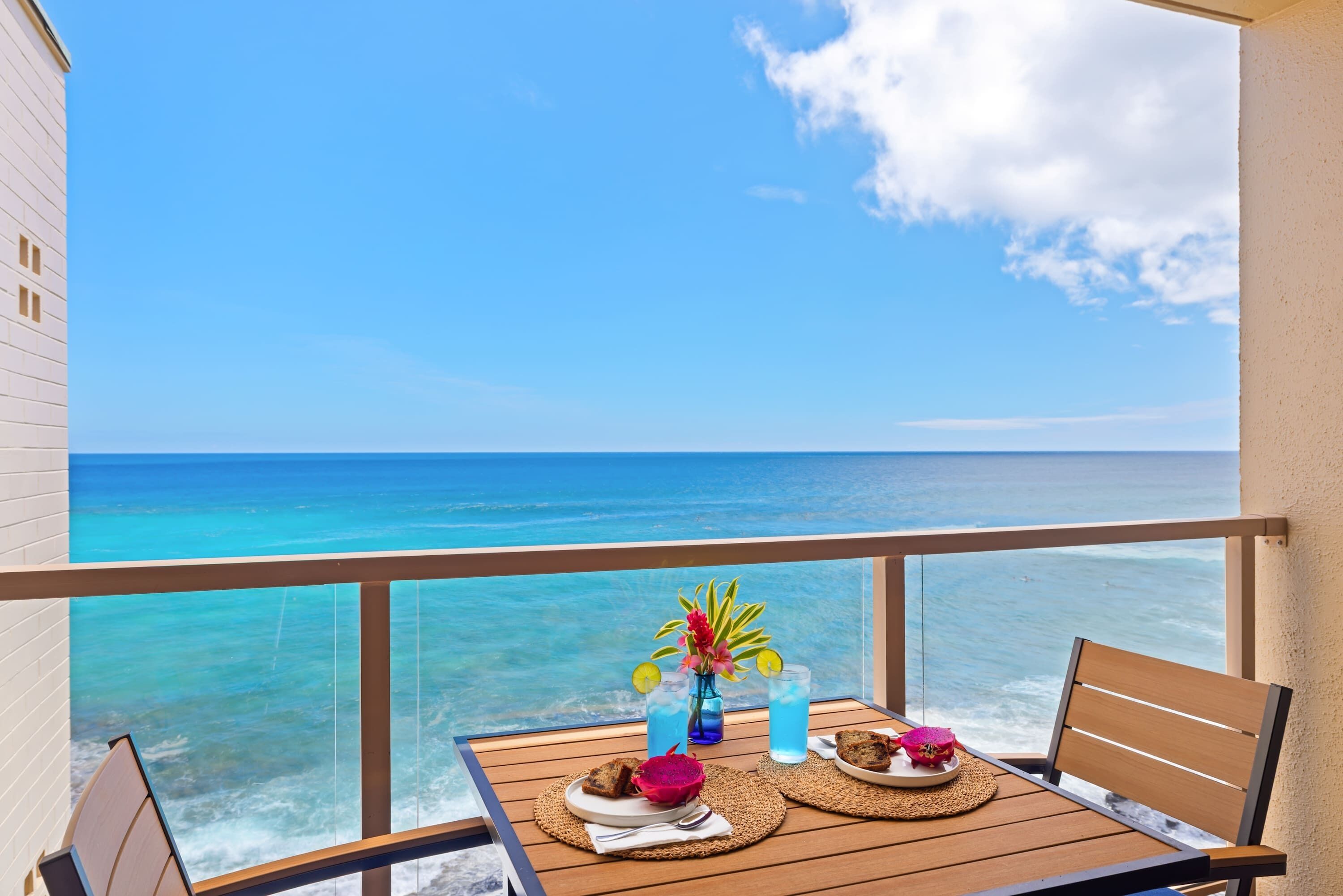 A balcony with a table set for two, overlooking a turquoise sea.