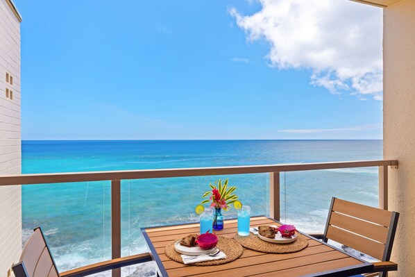 Un balcon avec une table dressée pour deux, donnant sur une mer turquoise.