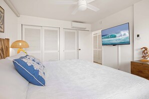 A bedroom with a bed, a television, a ceiling fan, and a wall-mounted air conditioning unit.