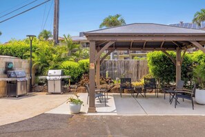 An outdoor patio with a covered seating area, two barbecue grills, and a stone wall.