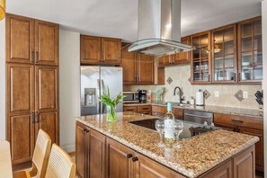 Cocina con armarios de madera, encimeras de granito, electrodomésticos de acero inoxidable y una isla integrada con lavaplatos y copa de vino.