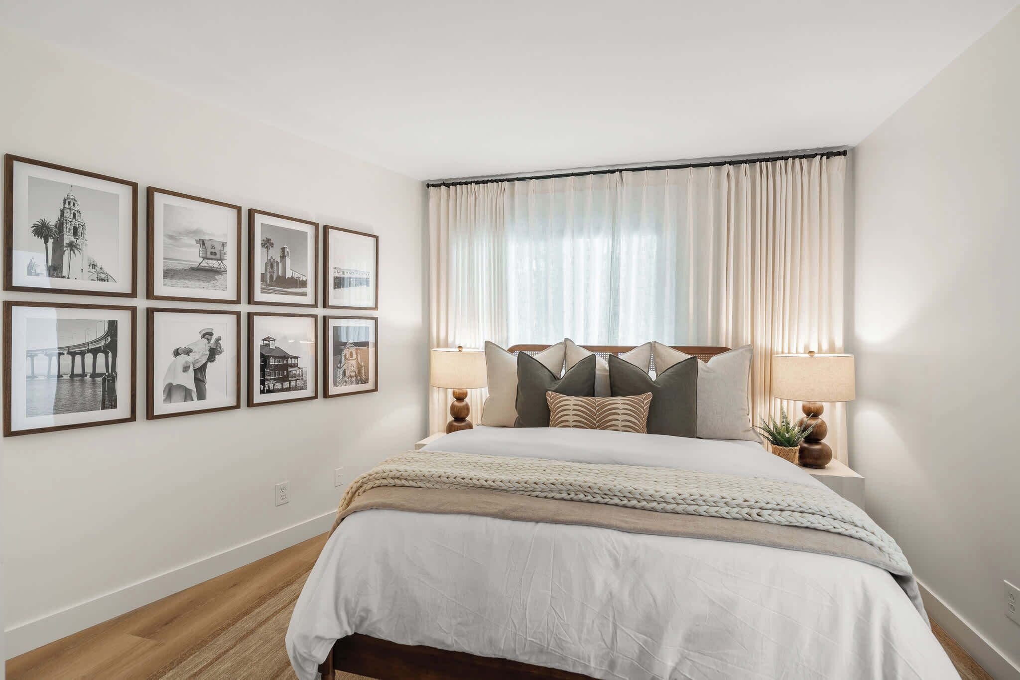 Een slaapkamer met een bed, een nachtkastje, een lamp en ingekaderde foto’s aan de muur.