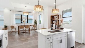 A modern kitchen with white cabinetry, a central island, and pendant lighting. - Sunset Oasis: Beachfront Bliss with 2 Pools, Fire Pits & Room for 16 (Melbourne Beach)