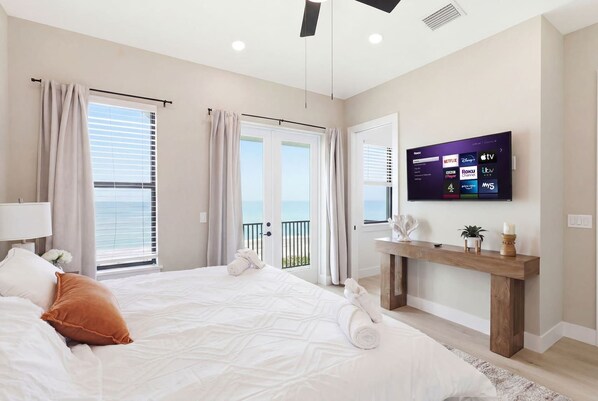 A bedroom with a bed, curtains, a TV, and a view of the sea. - Oceanfront Calm | Private Pool & Private Beach (Melbourne Beach)