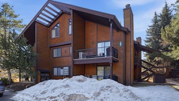 Un immeuble en bois à plusieurs étages, doté d’un balcon, d’un panneau indiquant un espace de stationnement et dont le sol est recouvert de neige.