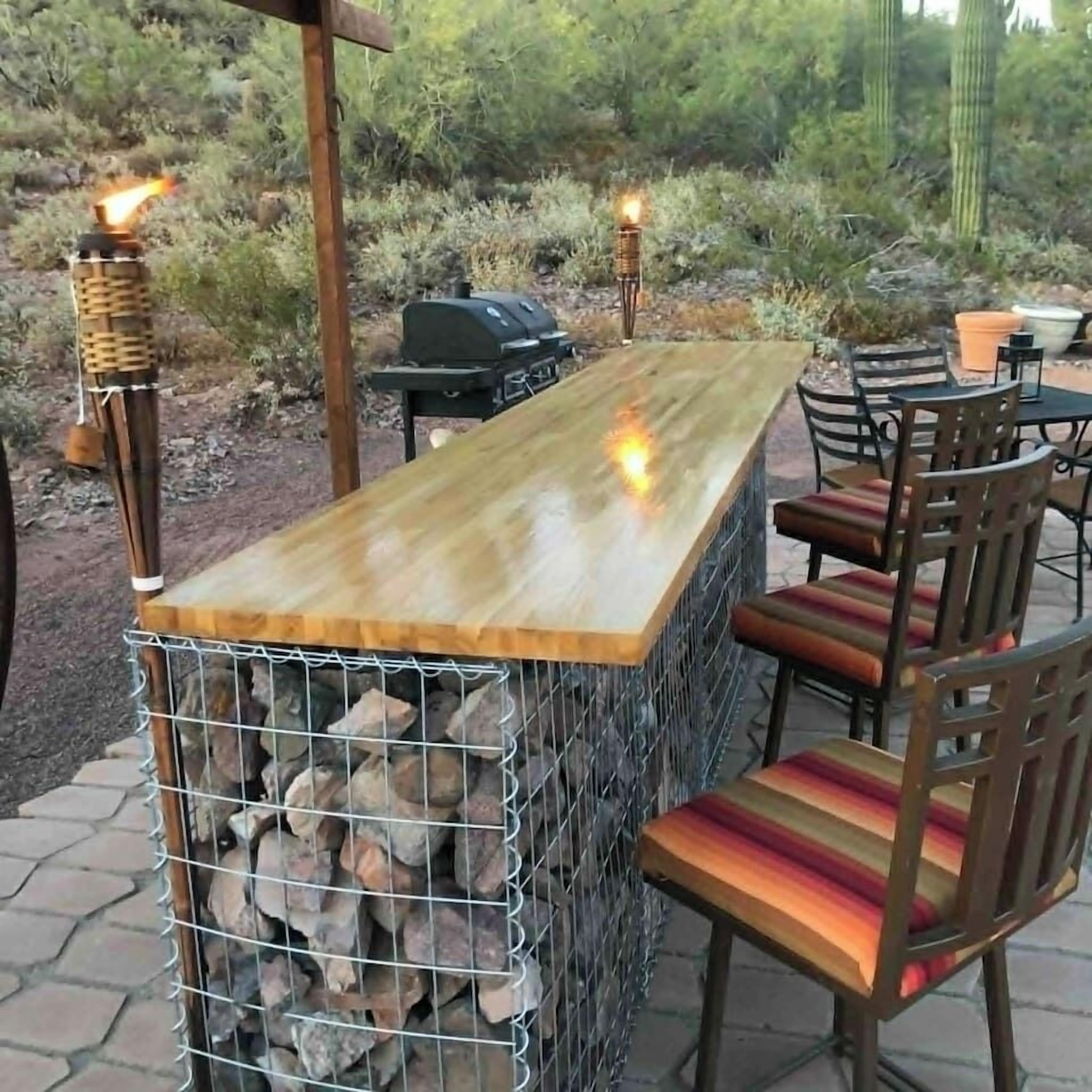 An outdoor bar area with a wooden counter, metal grill, and chairs.
