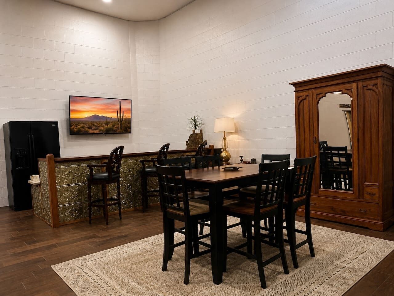 Un coin repas avec une table et des chaises en bois, un téléviseur fixé au mur, un meuble avec un miroir et un tapis à motifs sur le sol.