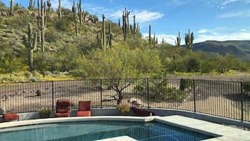 A pool with a surrounding fence, red chairs, and a desert landscape with cacti in the background.