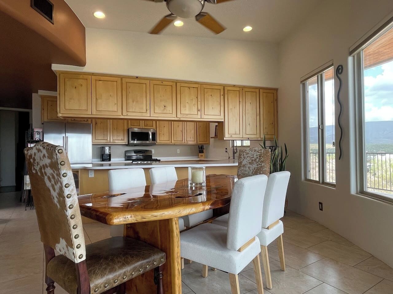 A modern kitchen with wooden cabinets, a central island, and a dining area with chairs.