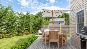 Una terraza con mesa y sillas, una parrilla y una valla de madera.