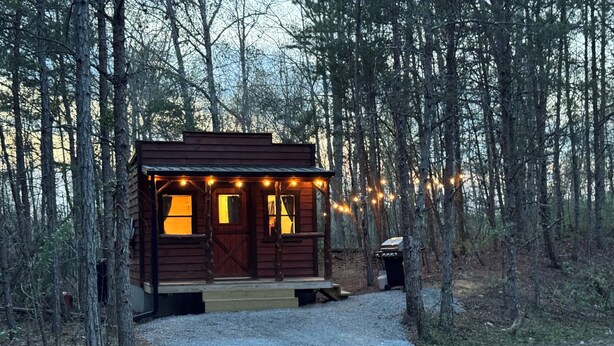 En stuga av trä med en veranda, omgiven av träd.
