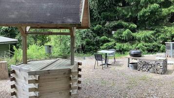 Un espacio de estar al aire libre con madera, que incluye una mesa, sillas, una parrilla y una estructura alimentada por energía solar.
