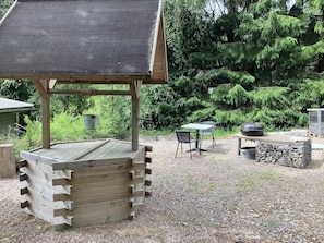 Un espacio de estar al aire libre con madera, que incluye una mesa, sillas, una parrilla y una estructura alimentada por energía solar.