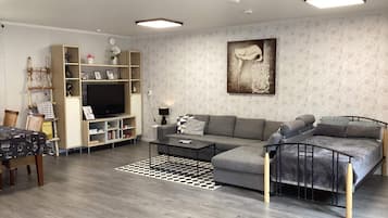 Uma sala de estar moderna com um sofá, uma mesa de centro e uma televisão. Há uma estante de livros e um quadro na parede.