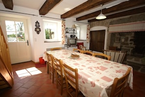 A dining area with a table set for six, wooden chairs, a window with curtains, a stone fireplace, and a door leading outside. - Charming Holiday Home With Enclosed Garden (Saint-Merd-la-Breuille)