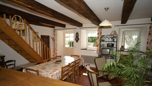 A dining area with a wooden staircase, a table with chairs, a television, and a potted plant. - Charming Holiday Home With Enclosed Garden (Saint-Merd-la-Breuille)