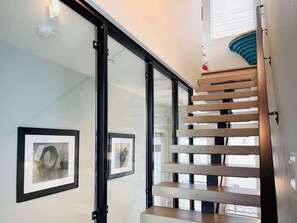 A modern staircase with glass railings and wooden steps, leading to a landing with framed artwork. - Sunset views with private terrace on Queen Anne (Seattle)