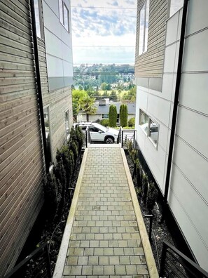 A narrow brick pathway leading to a building with a car parked outside. - Sunset views with private terrace on Queen Anne (Seattle)