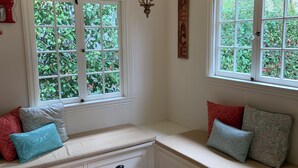 Quarto com área de estar com bancos embutidos, um candelabro e janelas com vista para o verde.