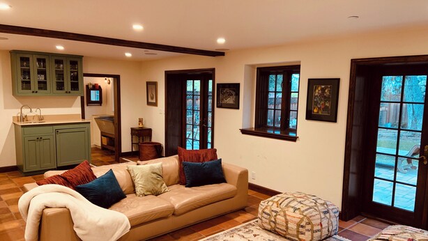 Sala de estar com sofá bege, tapete estampado e área de jantar com armários verdes.