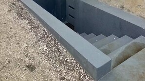 Een betonnen constructie met een wit rechthoekig platform, een metalen hek en een gebouw op de achtergrond.