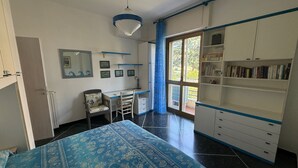 Een slaapkamer met een bed, bureau, stoel, kledingkast en uitzicht door een raam.