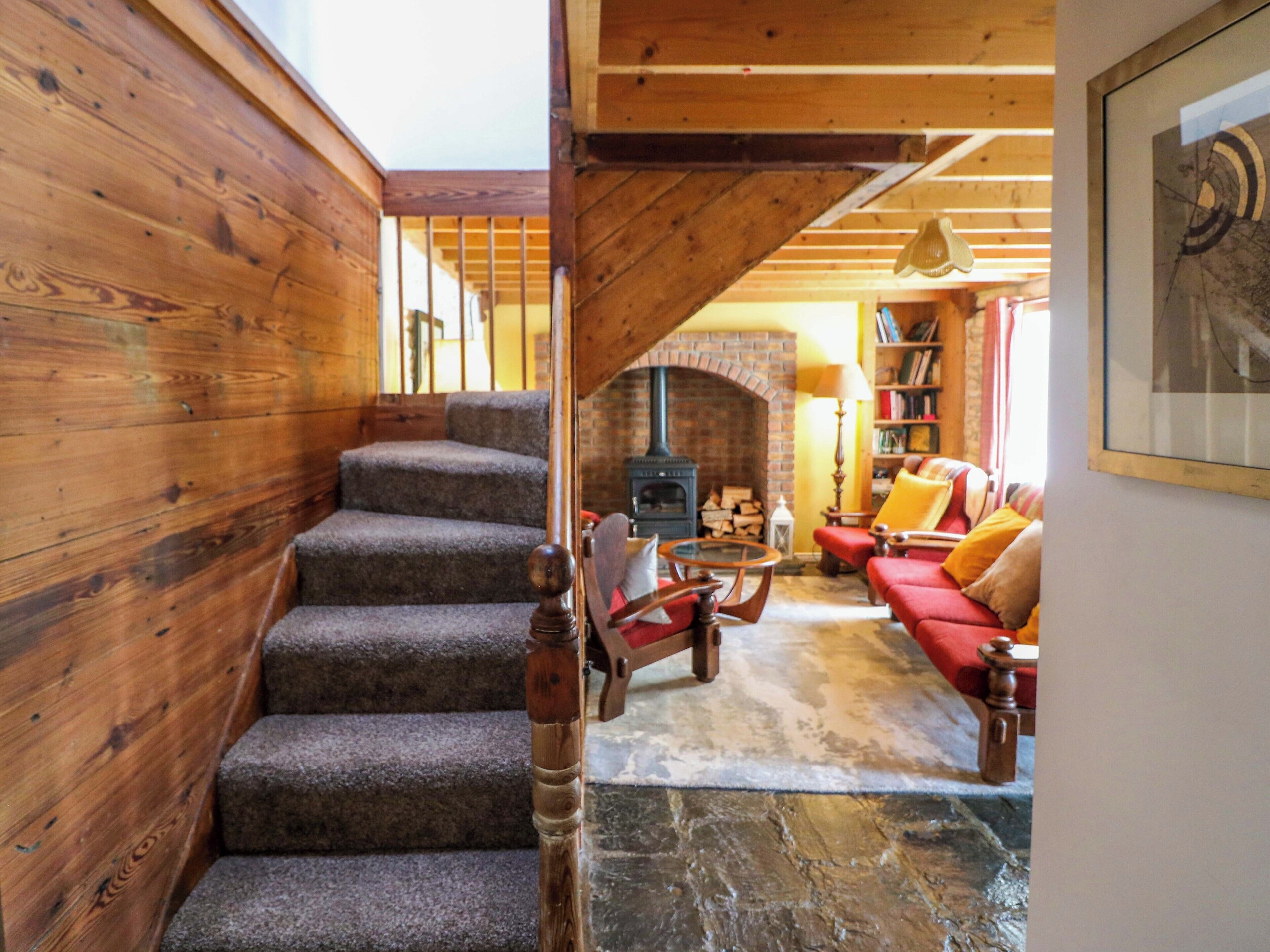 A wooden staircase leading to a living area with a fireplace, red sofa, and a bookshelf.
