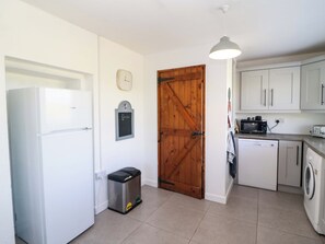Eine kleine Küche mit Kühlschrank, Waschmaschine und einer Holztür.