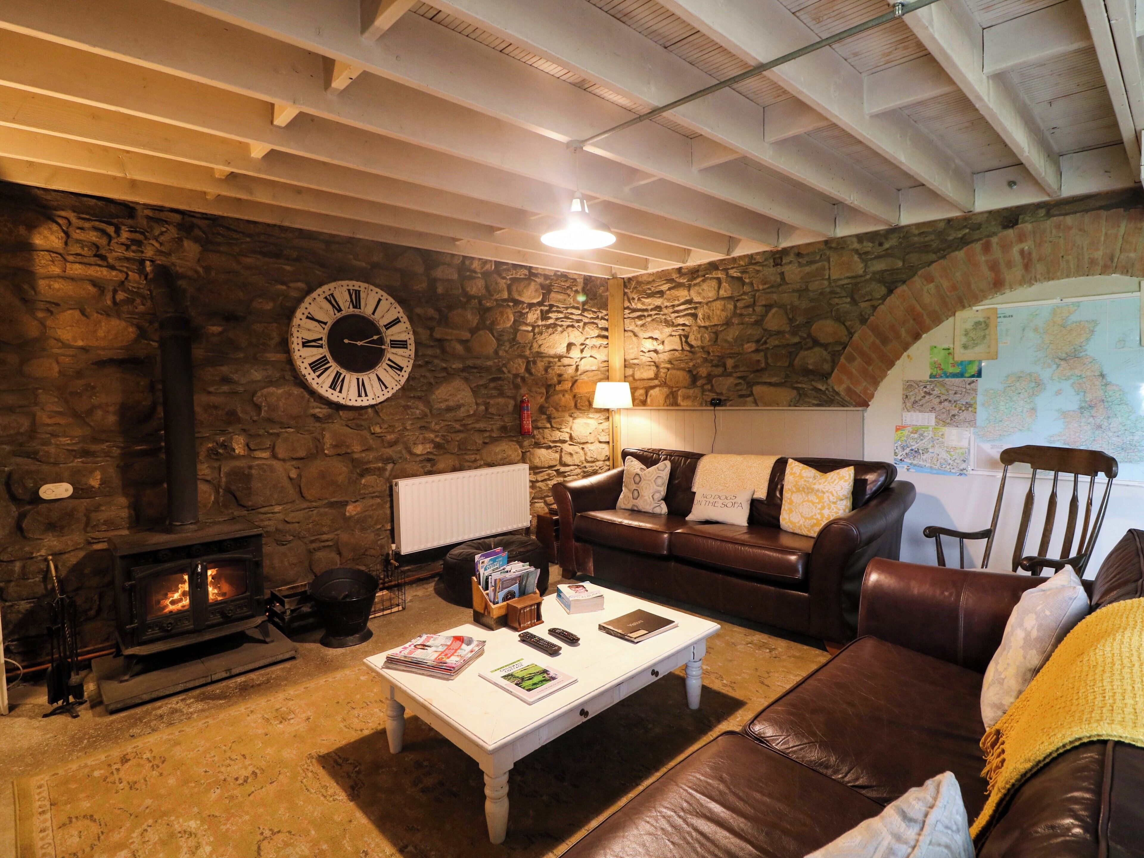 Ein gemütliches Wohnzimmer mit Steinwand, Kamin, Ledersofa, weißem Couchtisch und einer großen Uhr.