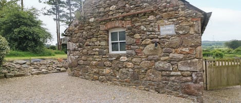 A stone cottage with a gravel driveway, a wooden gate, and a sign indicating 'Childwall Cottage.'
