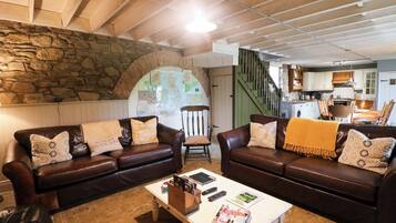 A cozy living room with leather sofas, a coffee table with magazines, and a stone wall.