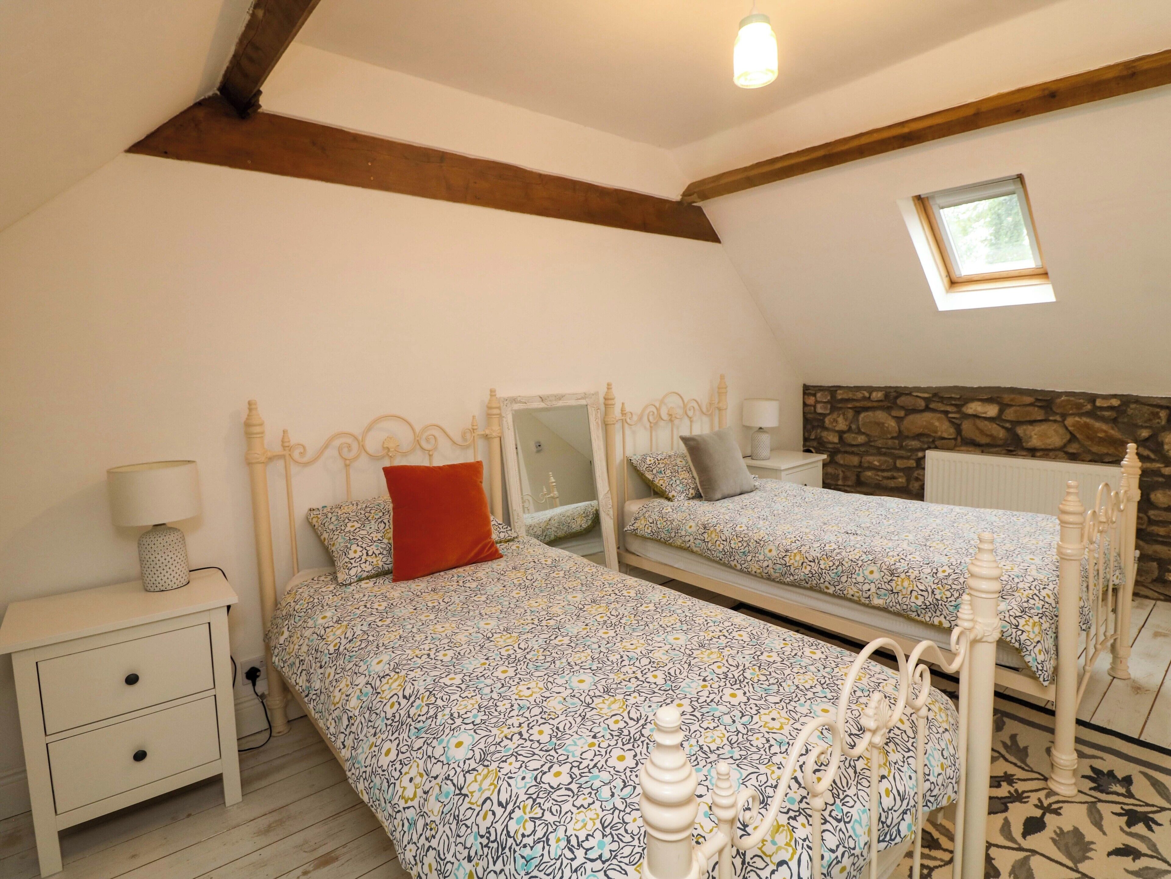 Une chambre avec deux lits, une table de chevet, une lampe, un mur en pierre et une lucarne.