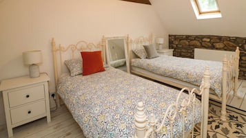 Une chambre avec deux lits, une table de chevet, une lampe, un mur en pierre et une lucarne.