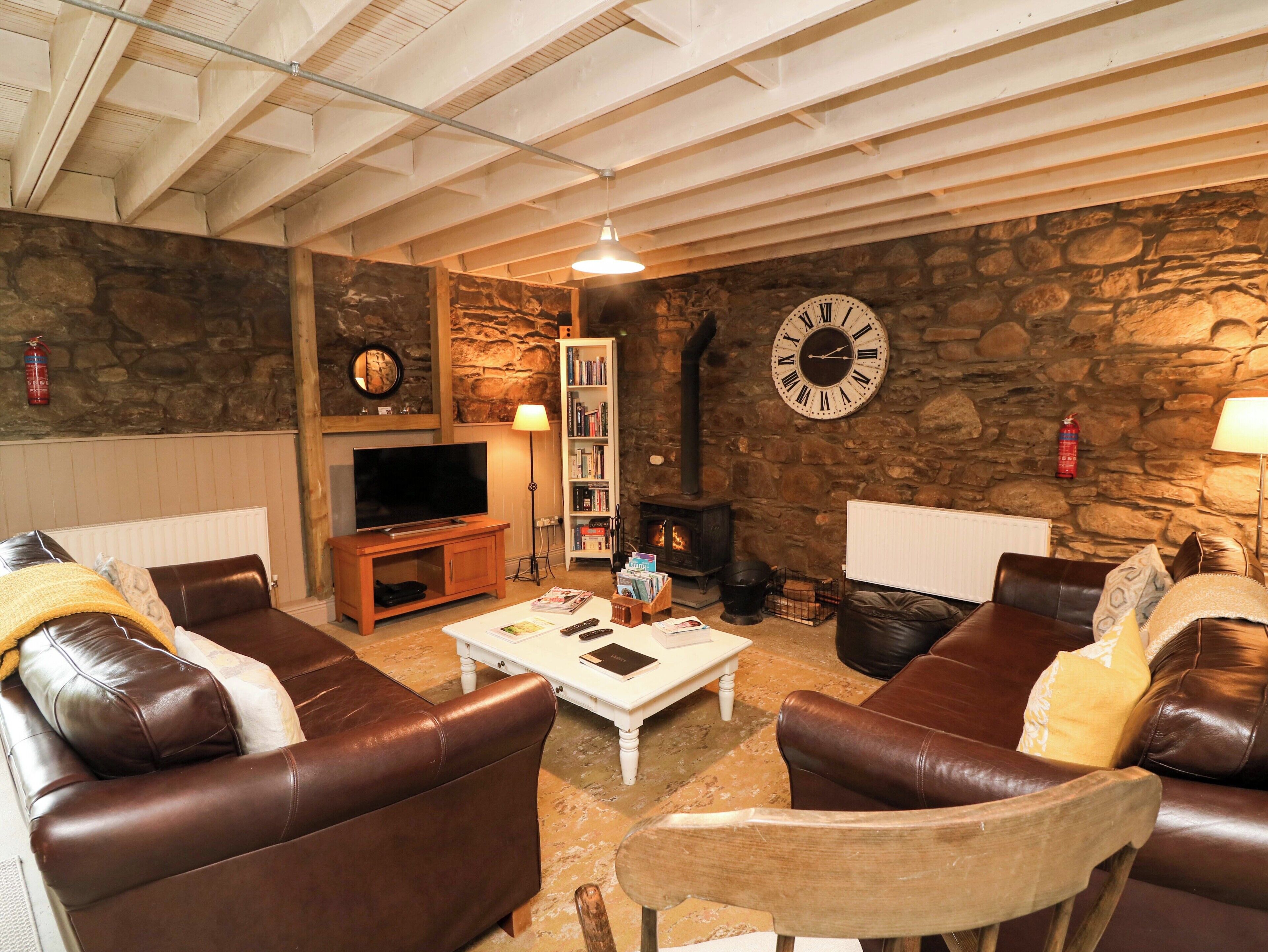 A cozy living room with leather sofas, a television, a bookshelf, a stone wall, and a fireplace.