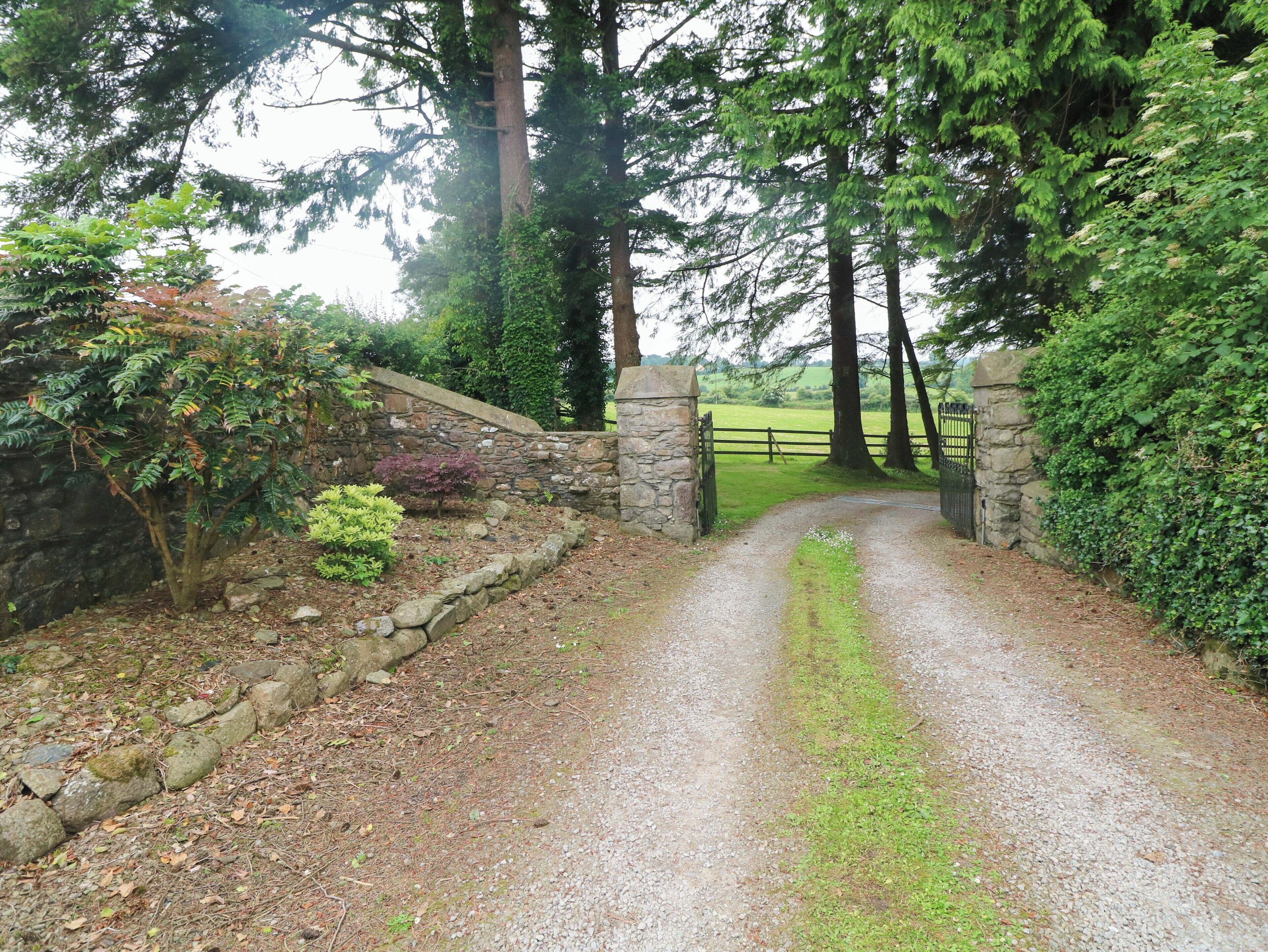 A gravel path leading to a stone gate with a stone wall on one side and a wooden fence on the other.