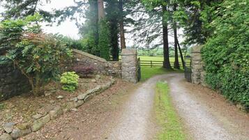 A gravel path leading to a stone gate with a stone wall on one side and a wooden fence on the other.