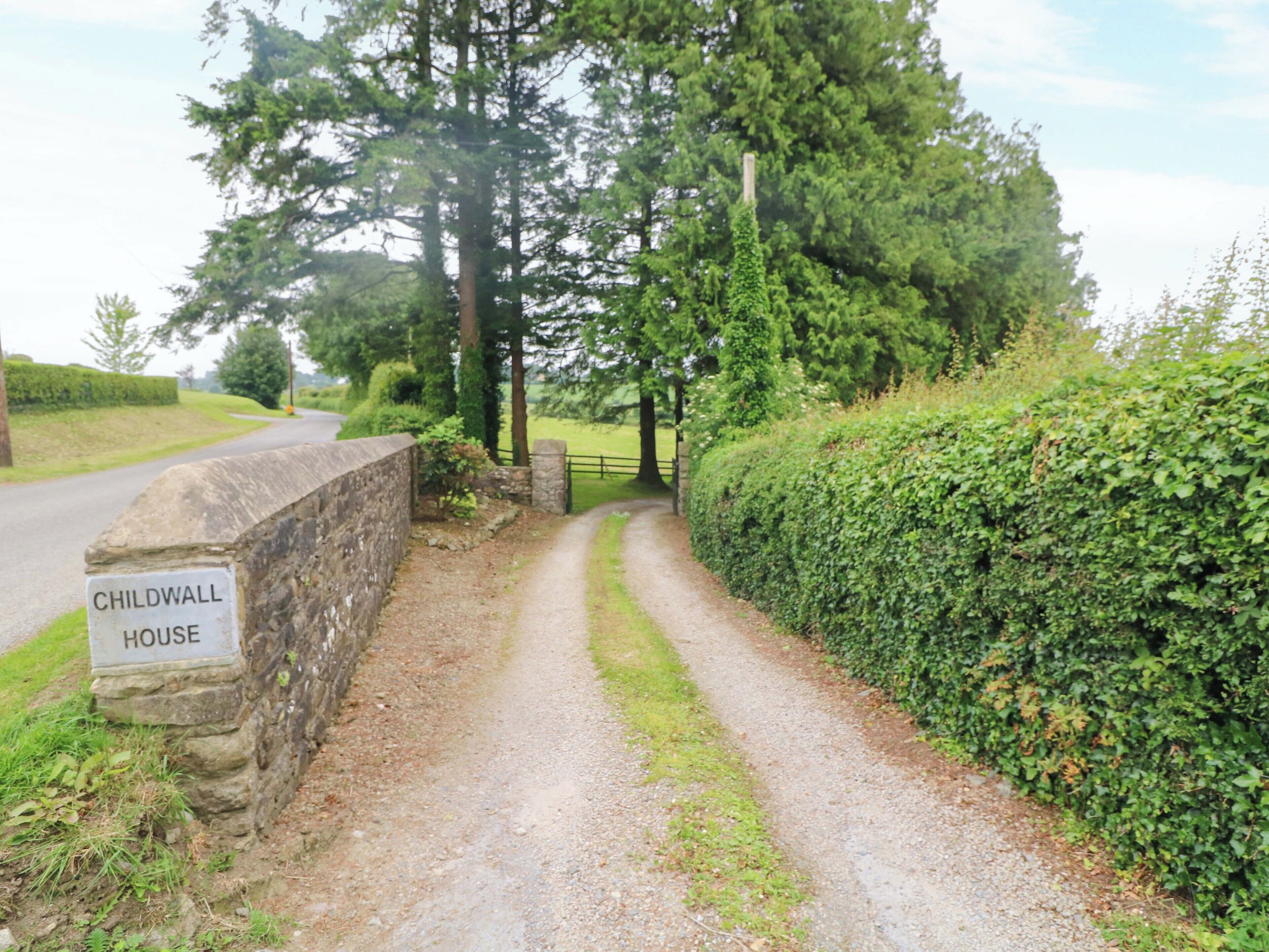 A rural road leading to a stone wall with a sign reading 'CHILDWALL HOUSE.'