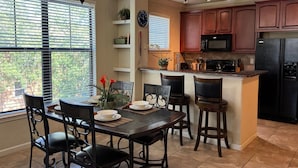 A kitchen with a dining area, featuring a central island, dark wooden chairs, a clock, and a microwave. - Spacious 3BR Retreat in Bella Piazza (DAVENPORT)