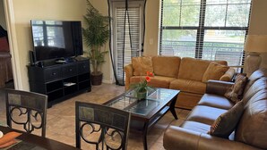 A living room with a TV, sofa, coffee table, chairs, and a potted plant. - Spacious 3BR Retreat in Bella Piazza (DAVENPORT)