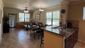A kitchen with a dining area, a ceiling fan, a clock, and a window with blinds. - Spacious 3BR Retreat in Bella Piazza (DAVENPORT)